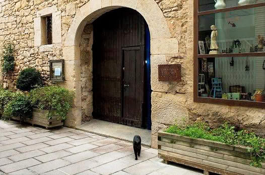 Façana de pedra del Museu de Cal Pauet, amb la porta d’arc, l’aparador i les jardineres